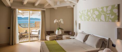 Ein Schlafzimmer mit Bett, grüner Decke, Blumen in einer Vase, einem Sessel, einem Tisch und Meerblick vom Balkon.