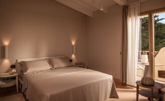 A bedroom with a large bed, bedside tables, a small table with a vase, and a view of the outdoors through a sliding door.