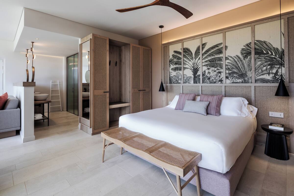 A modern bedroom with a large bed, a wooden bench, a wardrobe, and a wall-mounted artwork.