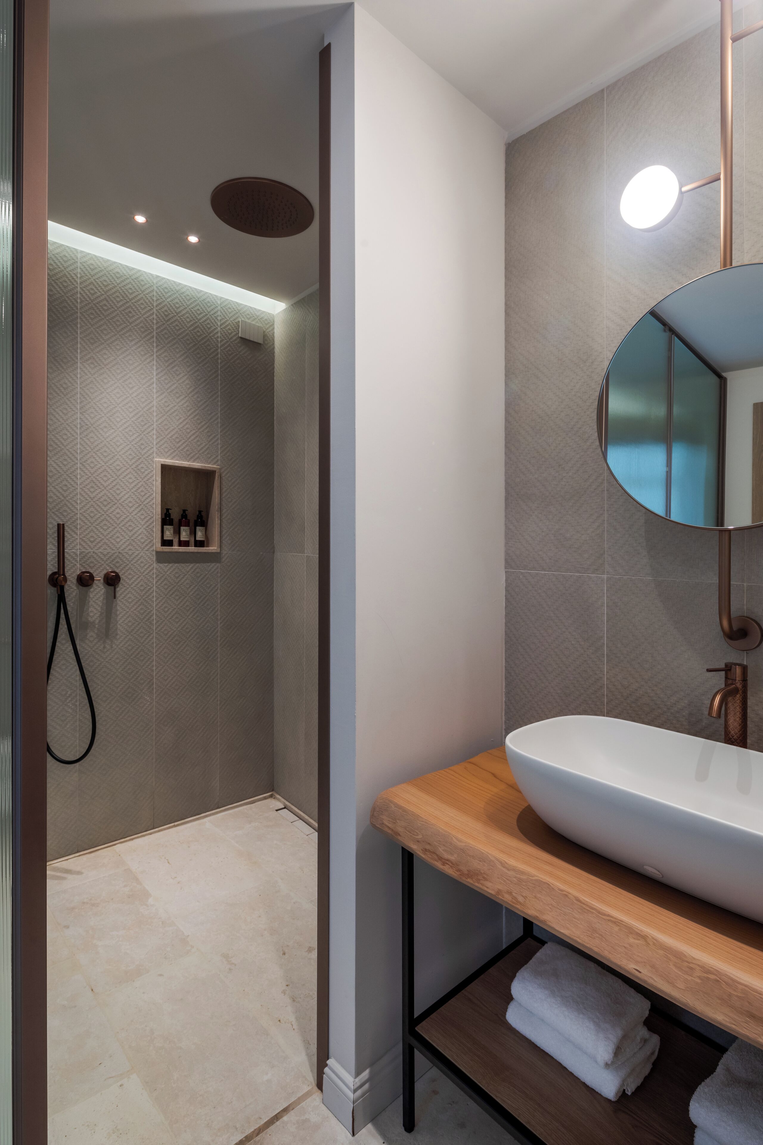 A modern bathroom with a wooden vanity, a large mirror, and a shower area with a textured wall.