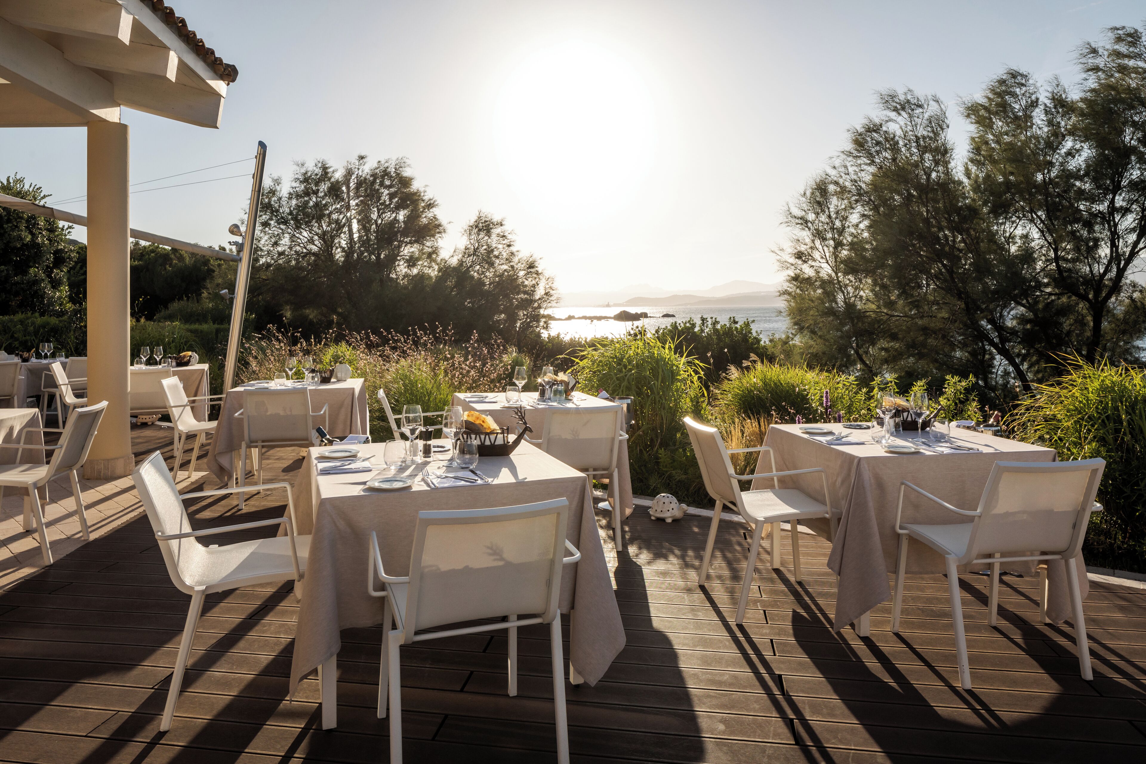 Un espace de restauration en plein air, avec des tables disposées pour deux personnes, entouré de verdure et offrant une vue sur un plan d’eau.