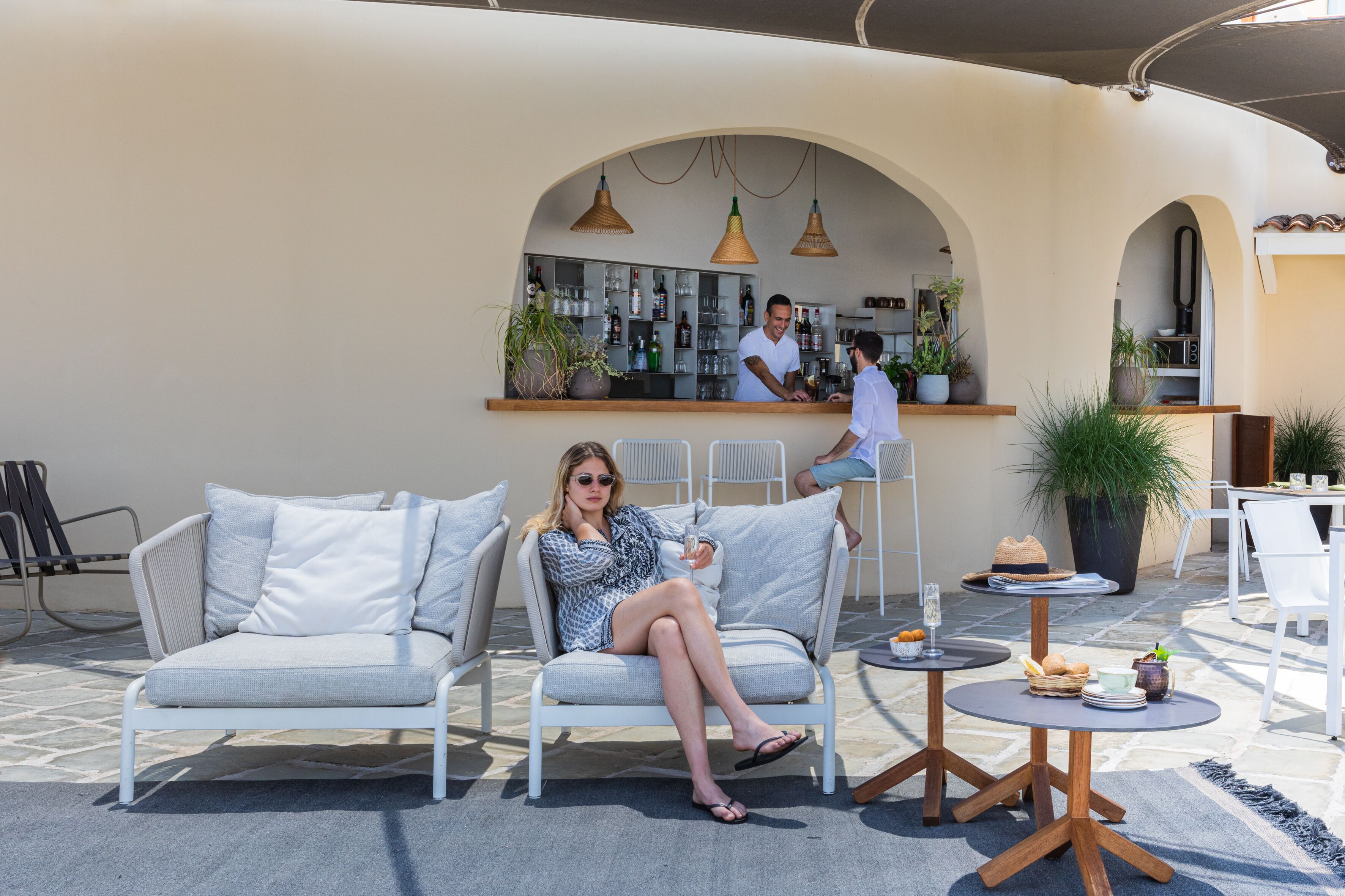 An outdoor seating area with a bar, white furniture, and potted plants.