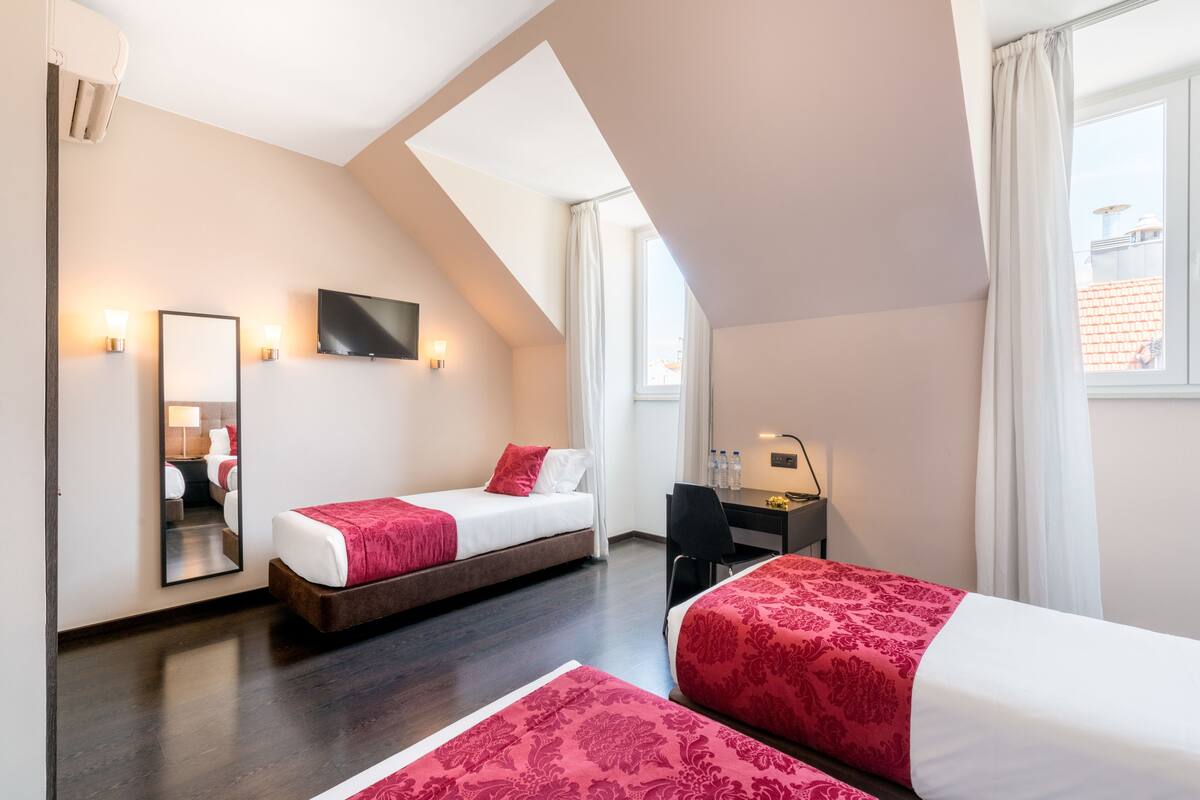 Een hotelkamer met twee bedden, een bureau, een stoel, een televisie en een groot raam.