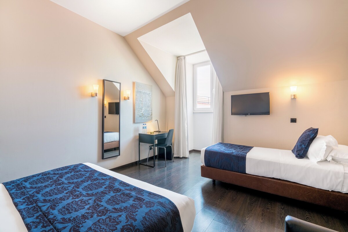 Une chambre d’hôtel avec deux lits, un bureau, une chaise, une télévision et une fenêtre avec des rideaux.