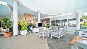 A spacious indoor area with seating arrangements, large windows, and potted plants. - Montebello Resort & Spa – All Inclusive (Fethiye)