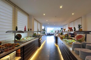 A buffet area with various food items and plates, a long counter, and a view of the dining area in the background.