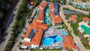 An aerial view of a resort with multiple swimming pools, a large central pool, and a variety of buildings with red-tiled roofs. - Montebello Resort & Spa – All Inclusive (Fethiye)