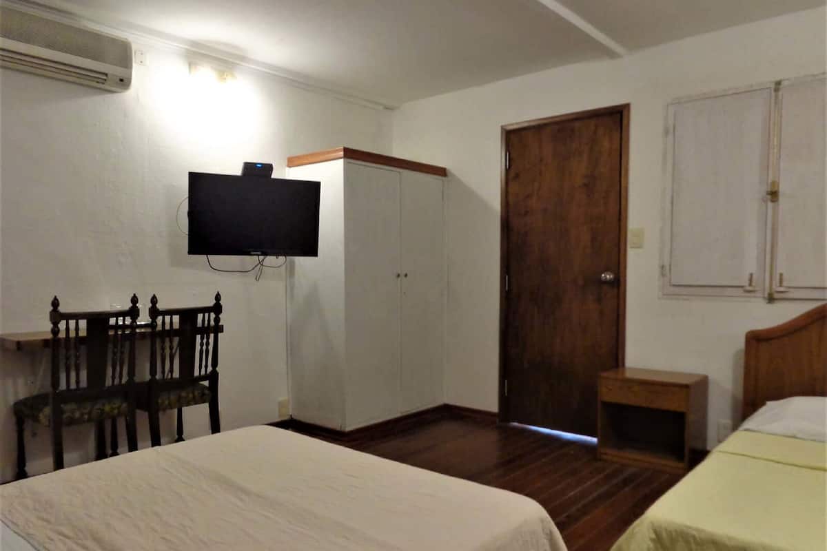 A room with two beds, a TV mounted on the wall, a wooden door, and a small table.