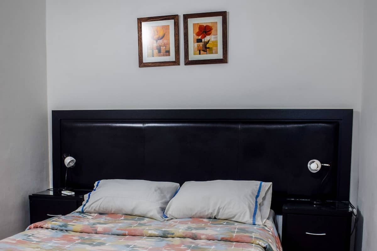 A bedroom with a bed, two bedside tables, a headboard, and two framed pictures on the wall.