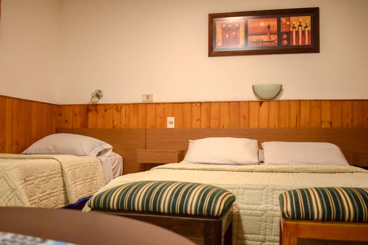A room with two beds, wooden paneling on the walls, a painting above the beds, and a small table with a bowl.