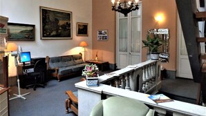 Een woonkamer met een bank, een bureau, een computer, een kroonluchter en een trap.