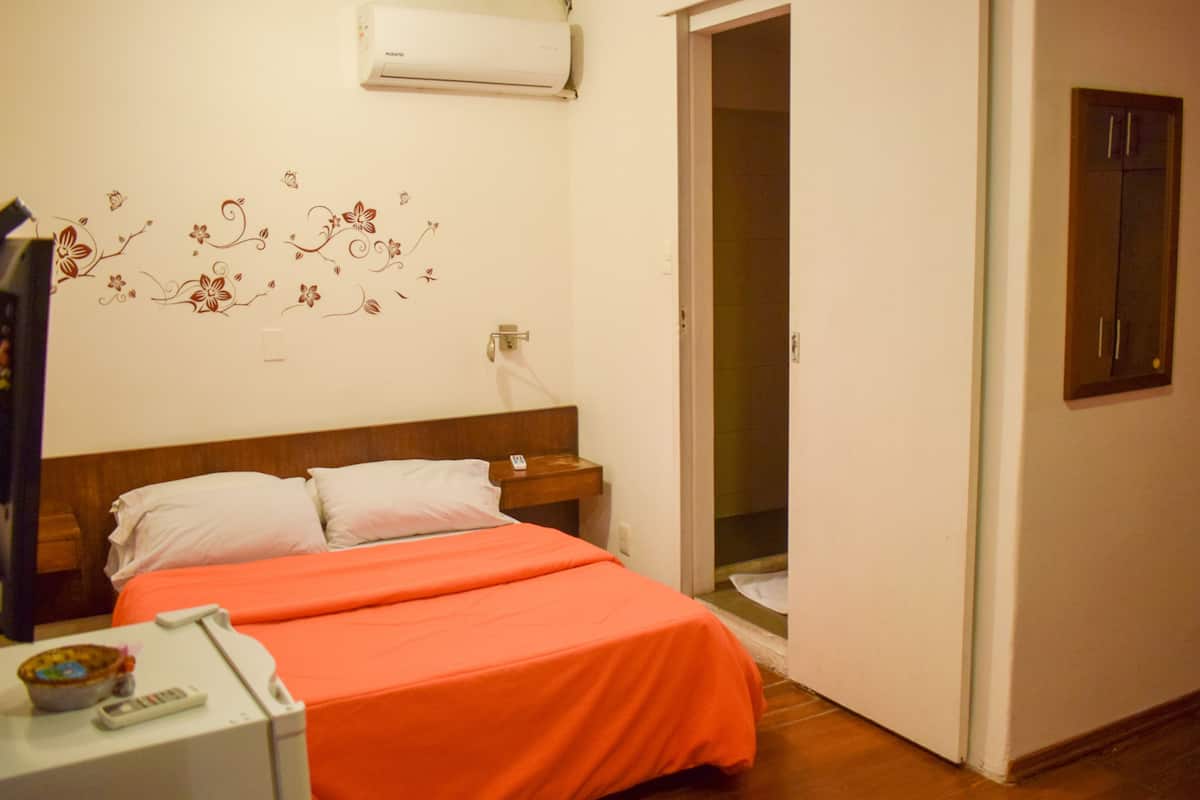 A bedroom with a bed, a nightstand, a wall-mounted air conditioner, and a door leading to another room.