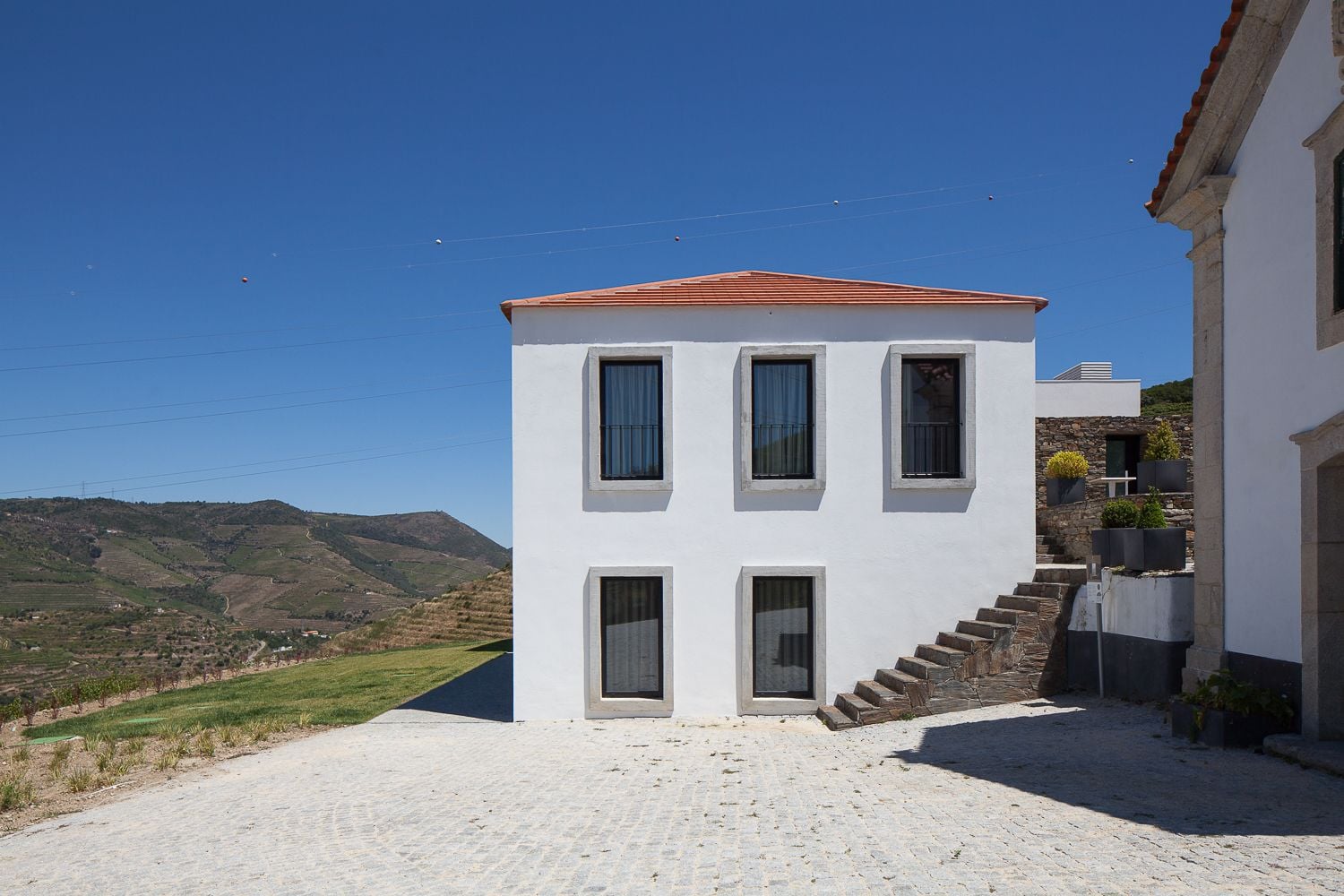 A two-story building with a red-tiled roof, a staircase leading to the upper floor, and a view of the surrounding landscape.