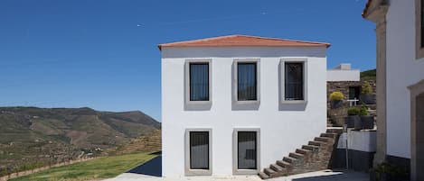 A two-story building with a red-tiled roof, a staircase leading to the upper floor, and a view of the surrounding landscape.
