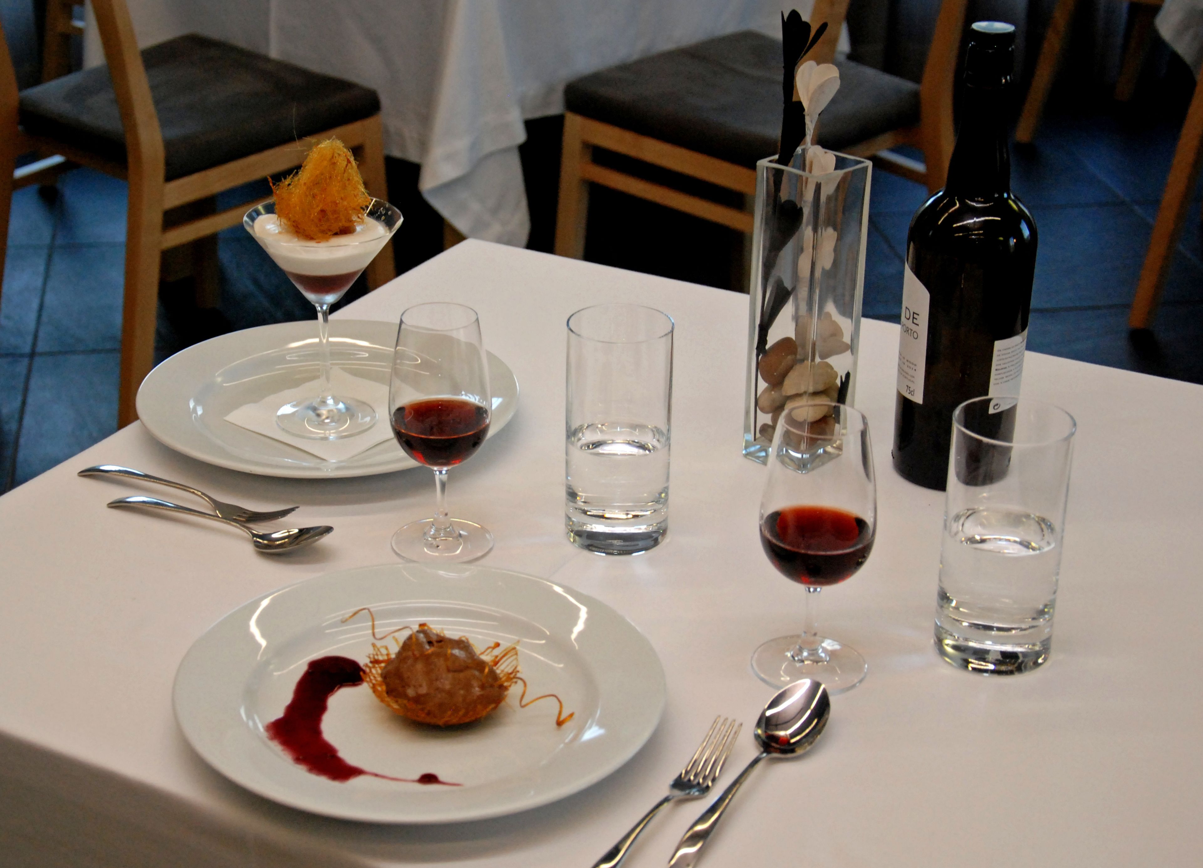 A dining table with plates, glasses, cutlery, and a bottle.