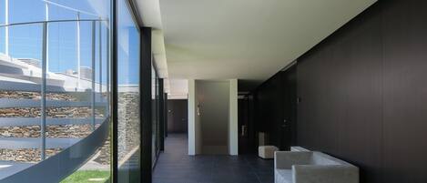 A modern hallway with a glass wall on one side, a dark interior, and a stone wall on the other.