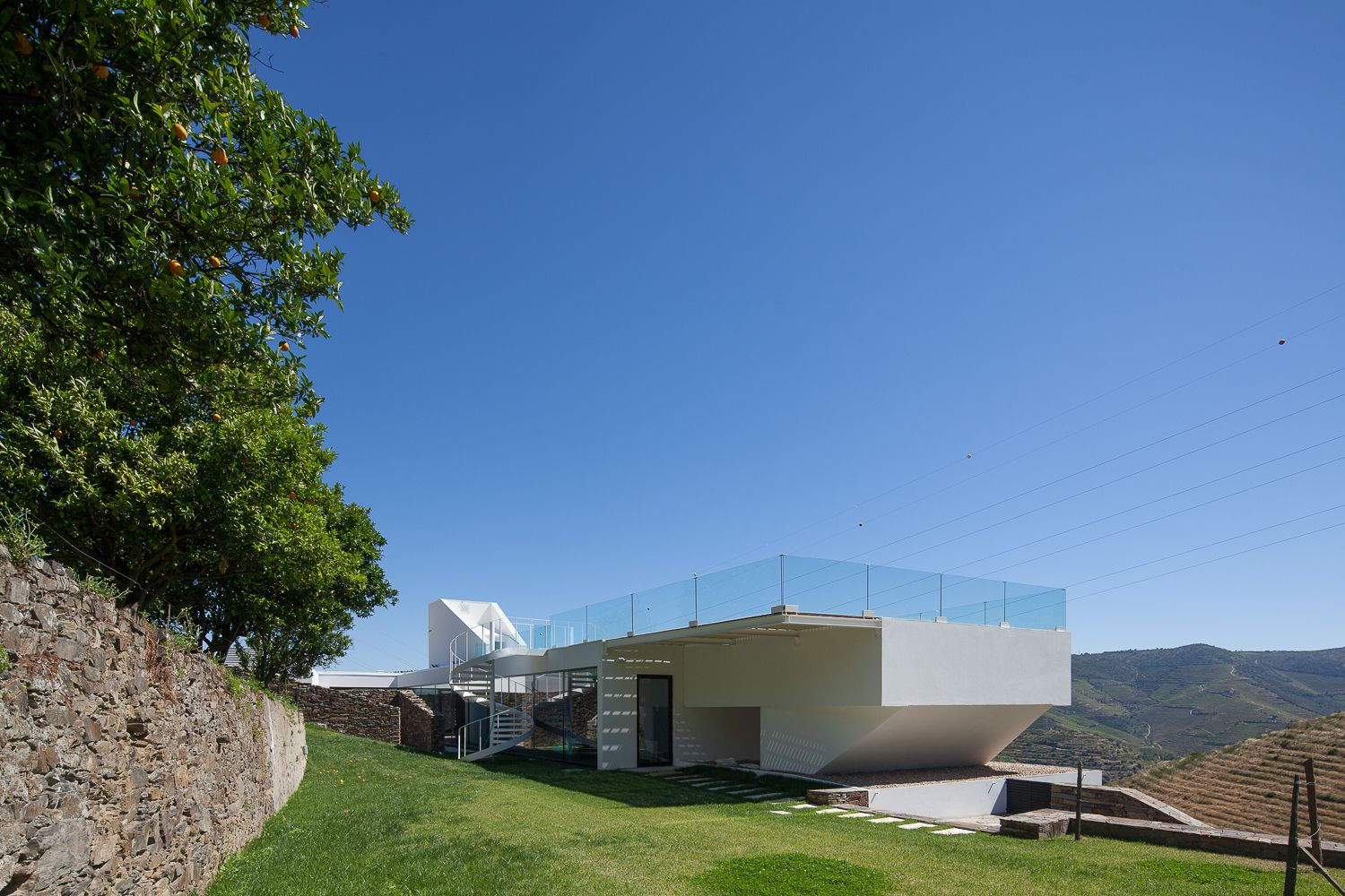 Ein modernes Gebäude mit Glasdach, Steinwand und einer Grünfläche.