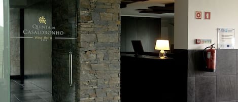 Zona de recepción con pared de piedra, mostrador de recepción, lámpara y extintor.
