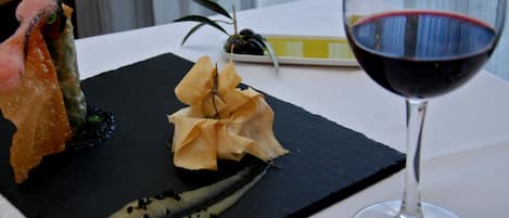 Una tabla de pizarra negra con un postre, una copa de vino tinto y una pequeña planta.