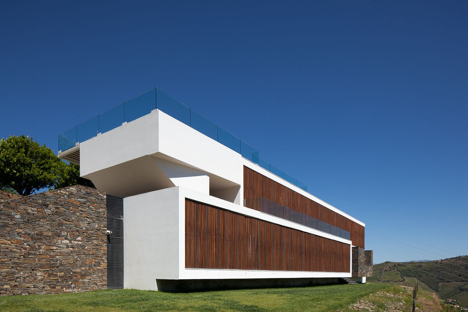 Una casa moderna con pared de piedra, fachada de madera y cielo azul despejado.