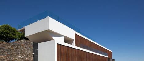 Una casa moderna con pared de piedra, fachada de madera y cielo azul despejado.