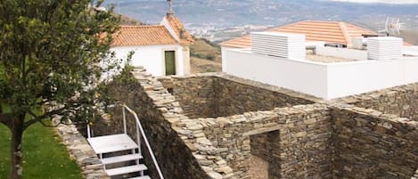 A stone-walled structure with a staircase leading to a white building with a tiled roof.