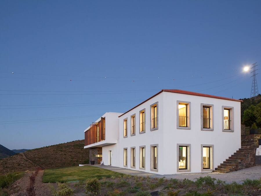Una casa moderna de dos pisos con varias ventanas, un techo rojo y una escalera de piedra que lleva a la entrada.
