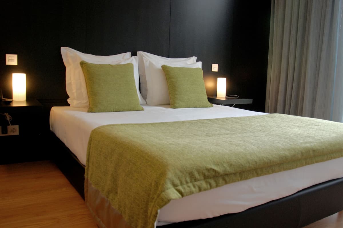 A neatly made bed with white linens and green pillows, a dark headboard, and bedside lamps.