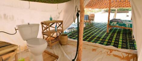 A tent with a toilet, a small table, and a chair.
