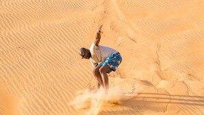 A person in a desert setting, wearing a grey shirt and patterned shorts, with sand being kicked up around them. - Ecolodge de Lompoul (Lompoul)