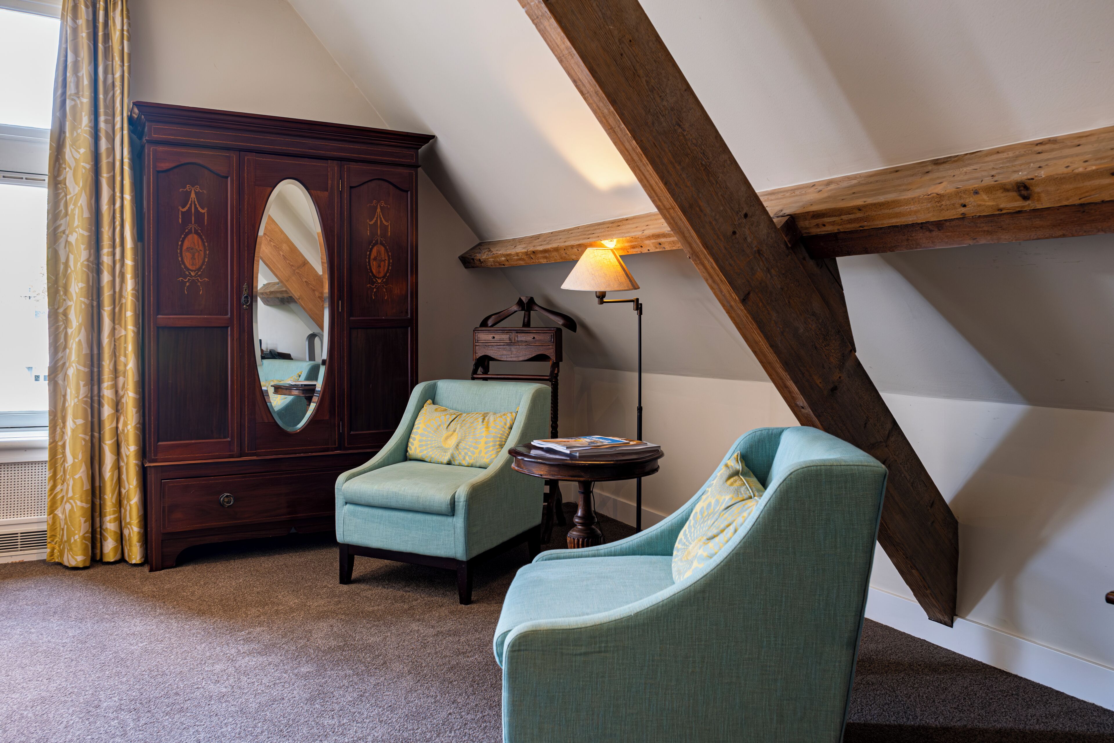 Een kamer met twee fauteuils, een houten kast en een lamp.