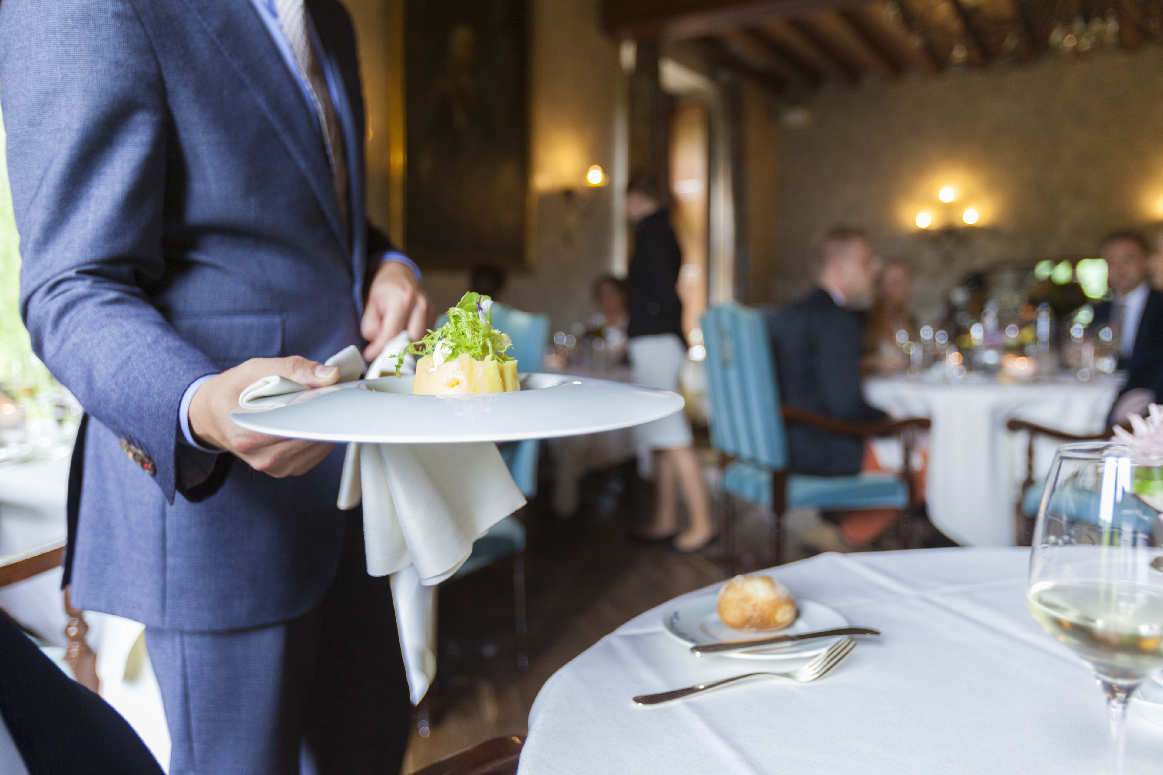 A waiter in a blue suit holding a white plate with a small dish of food.
