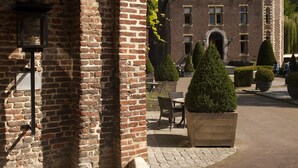 A historic building with a brick facade, an arched entrance, and a courtyard with potted plants and a bench. - Van der Valk Hotel Kasteel Terworm (Heerlen)