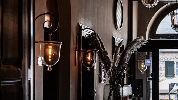 A corridor with wall-mounted sconces, a piano, and a decorative plant. - Van der Valk Hotel Kasteel Terworm (Heerlen)
