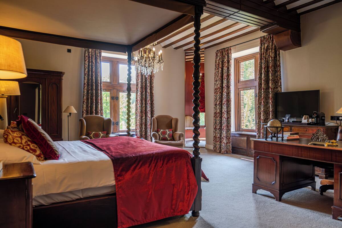 A bedroom with a four-poster bed, a desk with a television, and a chair.