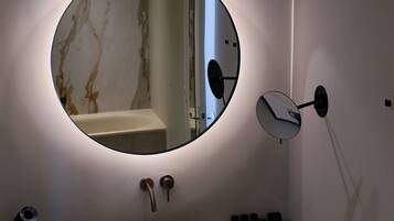A bathroom with a round mirror, a sink, a towel rack, and a wall-mounted light fixture.