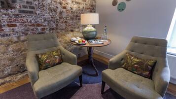 A room with two armchairs, a round table with a lamp, and a brick wall.