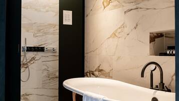 A modern bathroom with a freestanding bathtub, a shower area, and marble walls.
