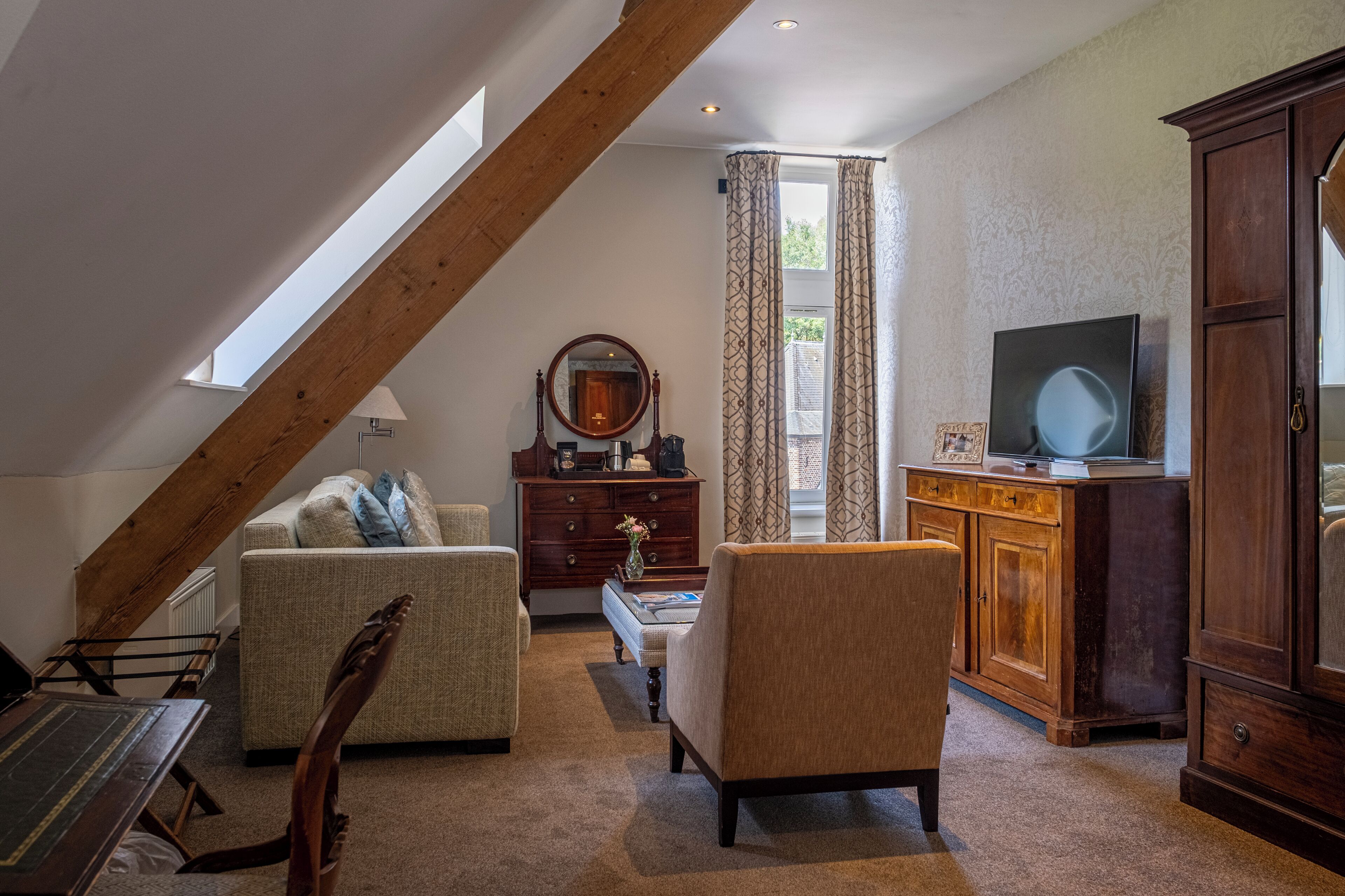 Een loft-achtige kamer met een schuine plafond, een bank, een stoel, een houten kast en een televisie.