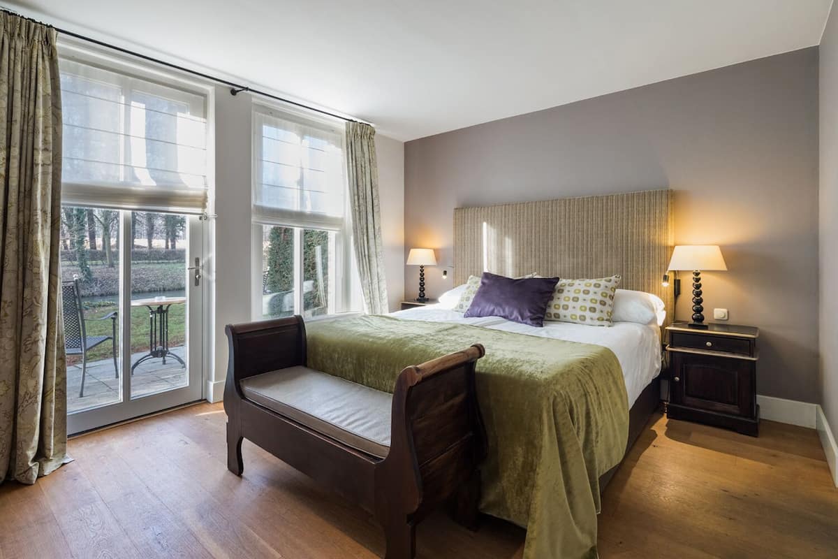 A bedroom with a bed, two bedside tables, a bench, and a view of the outdoors through a sliding glass door.
