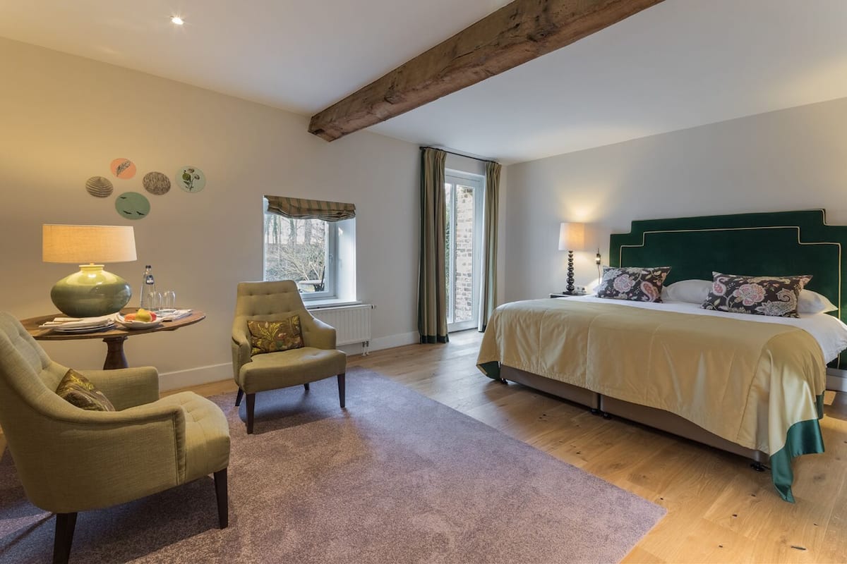 A bedroom with a large bed, a chair, a table with a lamp, and a window with curtains.