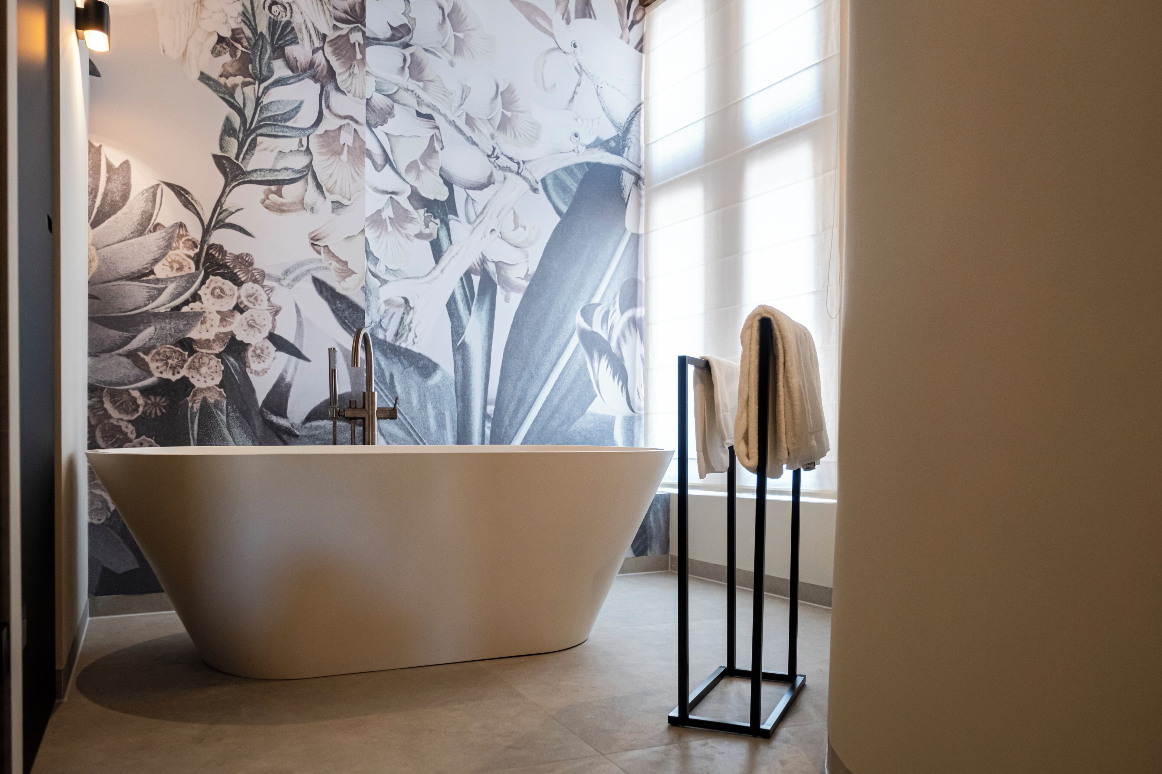 A modern bathroom with a freestanding bathtub, a towel rack, and a floral wallpaper.