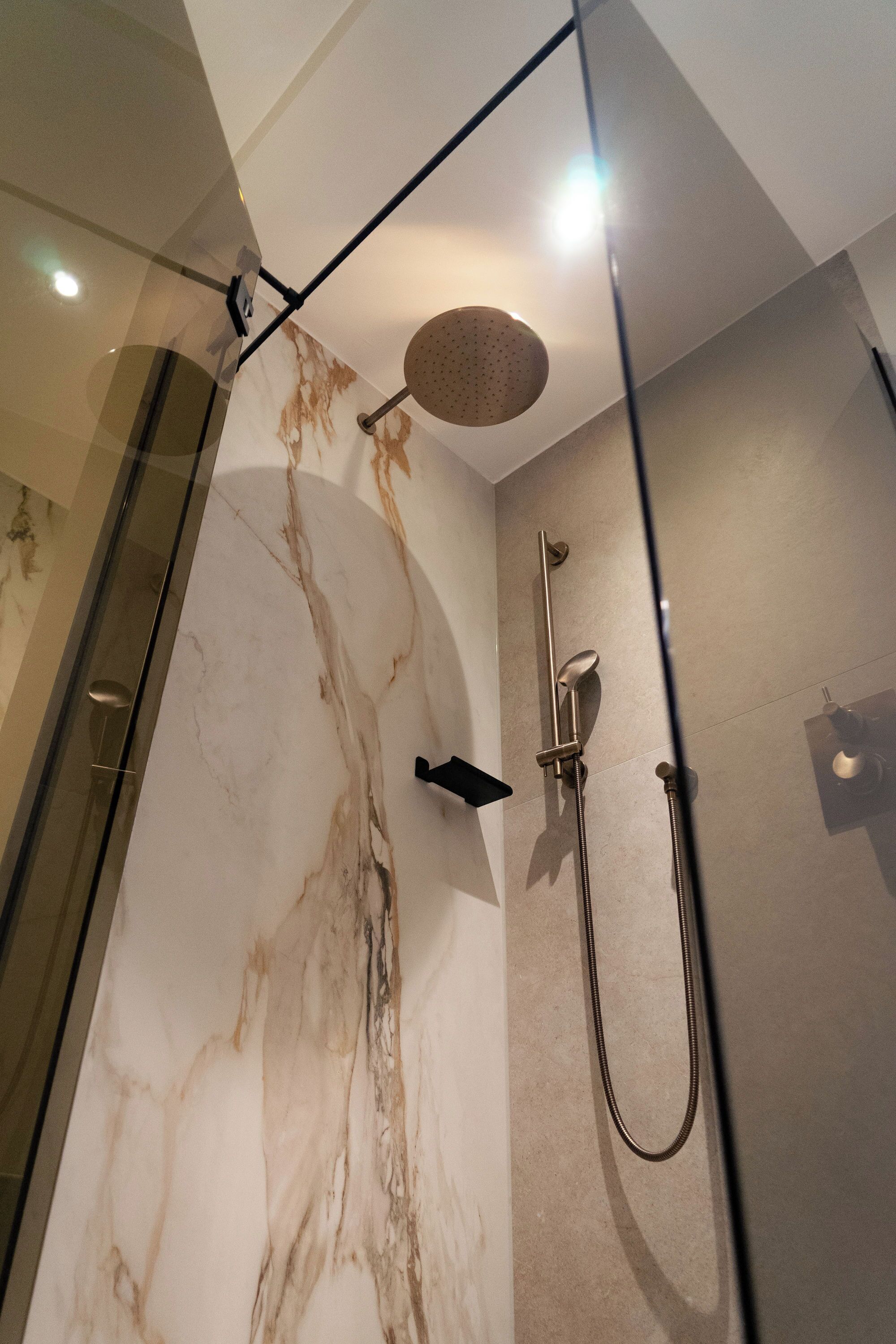 A modern bathroom with a glass shower enclosure, a marble wall, and a handheld showerhead.