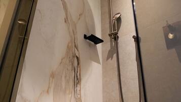A modern bathroom with a glass shower enclosure, a marble wall, and a handheld showerhead.