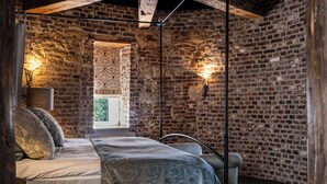 A bedroom with a brick wall, a bed with a grey blanket, and two wall-mounted lights. - Van der Valk Hotel Kasteel Terworm (Heerlen)