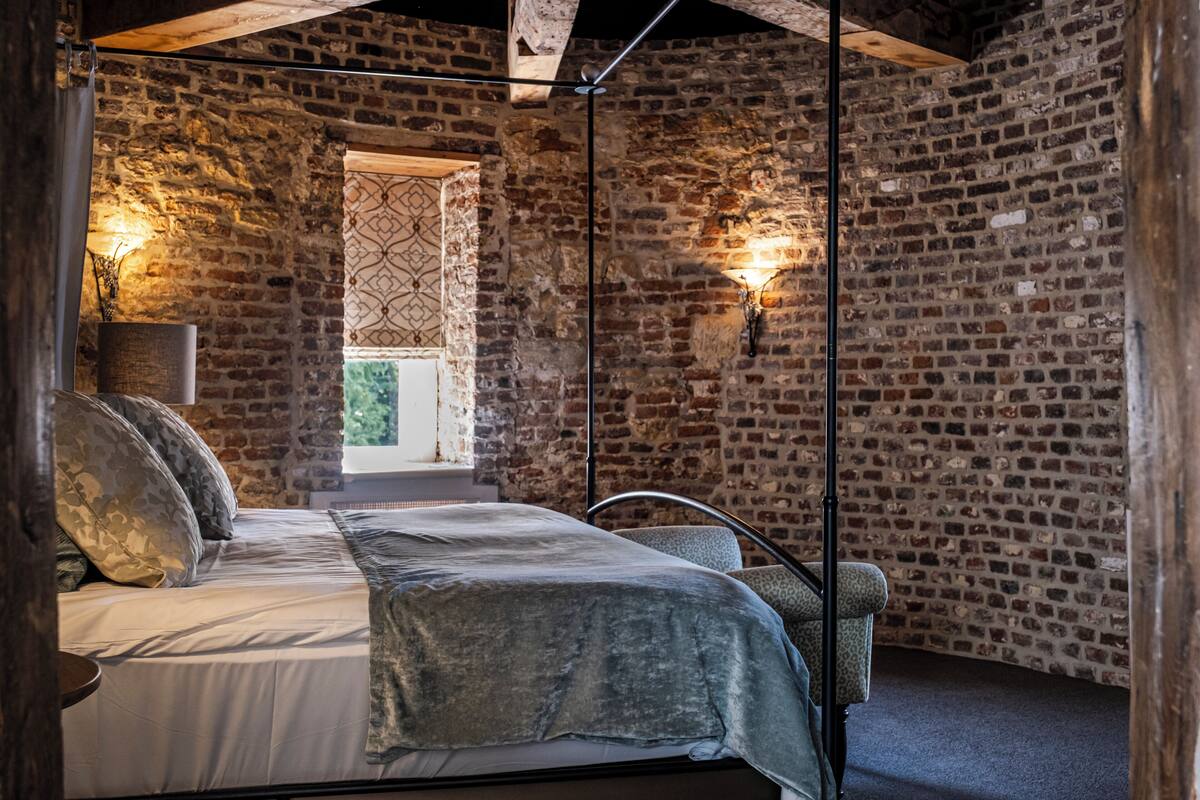 A bedroom with a brick wall, a bed with a grey blanket, and two wall-mounted lights.