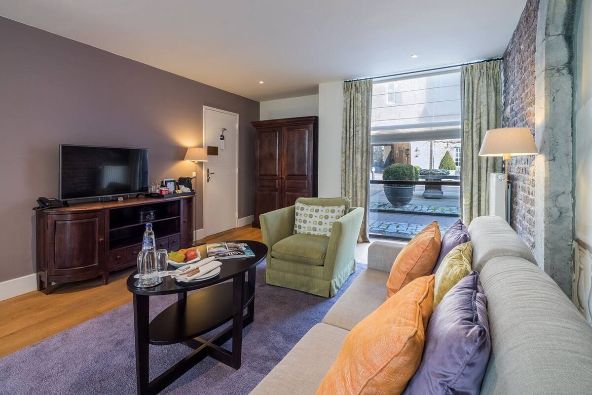 A living room with a sofa, armchairs, a coffee table, a TV, and a window with curtains.