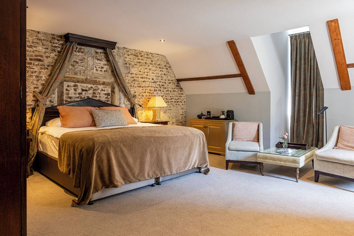A bedroom with a large bed, a nightstand, a lamp, a chair, and a desk.