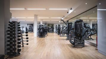 A gym with various exercise machines, wooden flooring, and a mirrored wall.