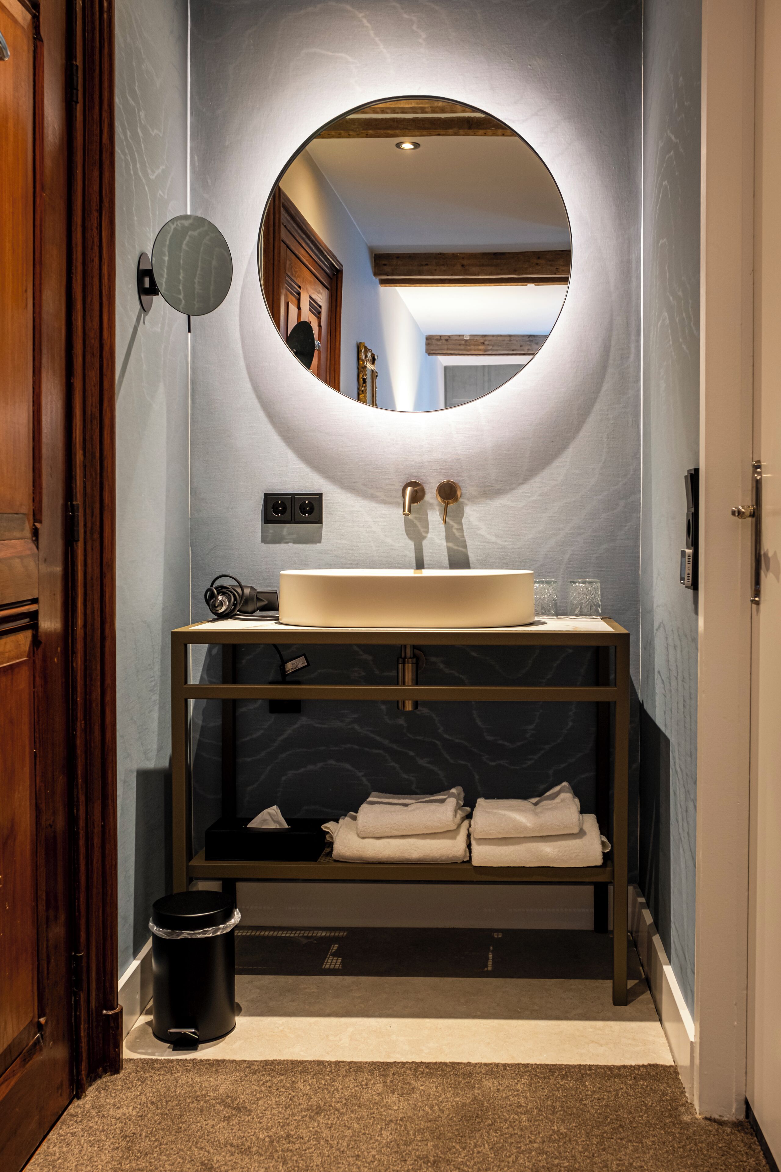 A bathroom with a round mirror, a sink, and a vanity with towels.